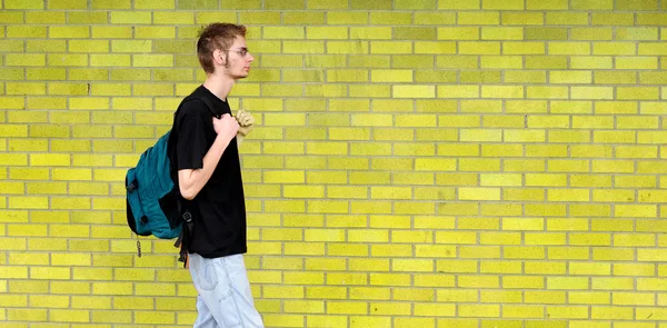 Estudante caminhando além da parede de tijolo — Fotografia de Stock