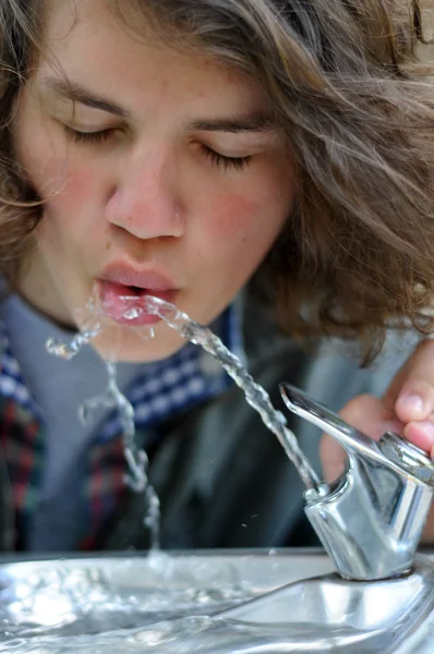 stock image A young white Caucasian adult teen drinks from a public drinking fountain
