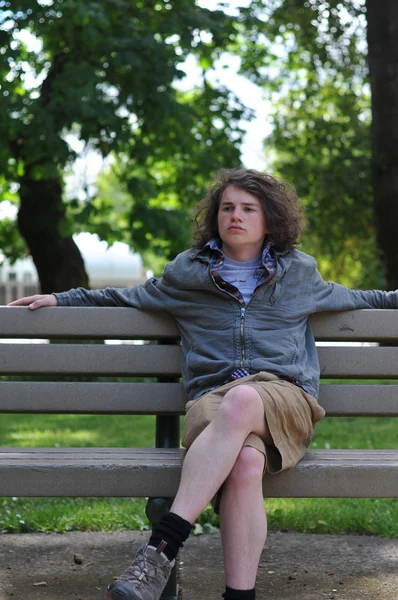Подросток сидит на скамейке и расслабляется, думая: — стоковое фото