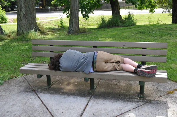 stock image A homeless person takes a nap on a bench in a public park.