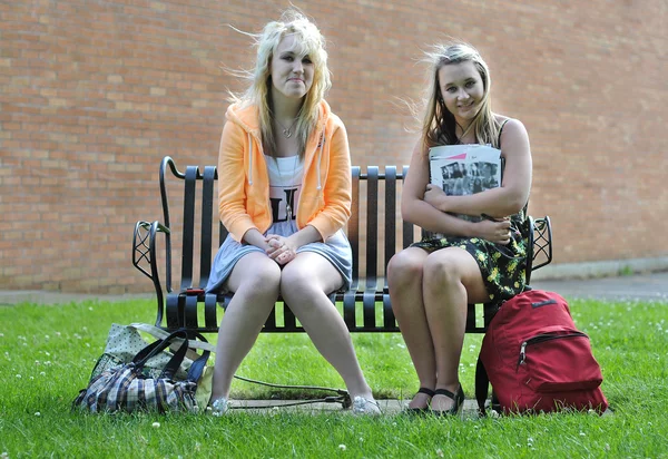 人の十代女の子友人建物のそれらの横にある彼らの袋でお互いに勉強し 話しているベンチに高等学校の前に座っています — ストック写真