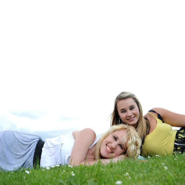 关闭两个可爱的年轻少女躺在草微笑着和大家一起开怀大笑 — 图库照片