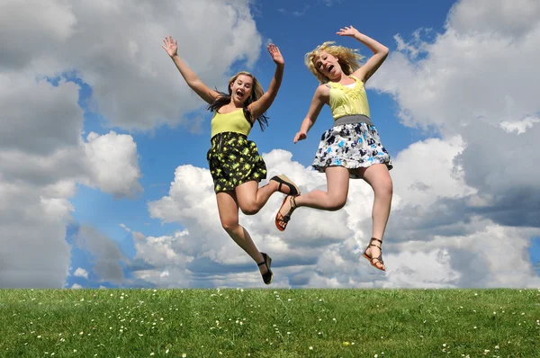 Kaksi Nuorta Tyttöä Hyppää Ruohikkokukkulan Yli Kädet Ylhäällä Sinisen Taivaan — kuvapankkivalokuva