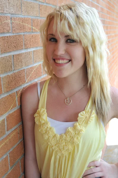 Dívka stojící vedle cihlová zeď s úsměvem — Stock fotografie