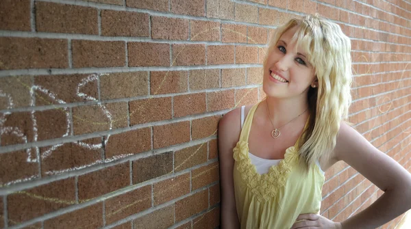 Meisje permanent naast een bakstenen muur glimlachen — Stockfoto