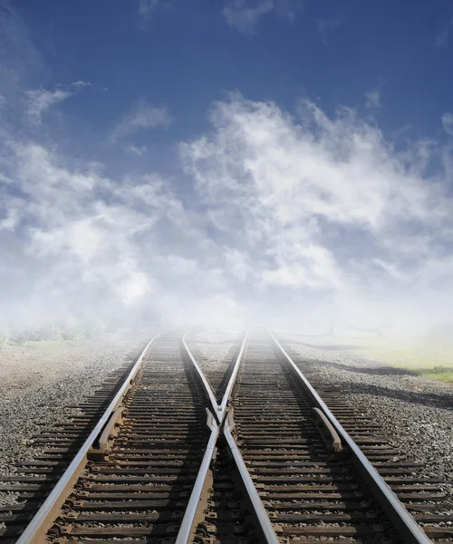 stock image Two railroad tracks lead off into the daylight foggy sky with clouds.