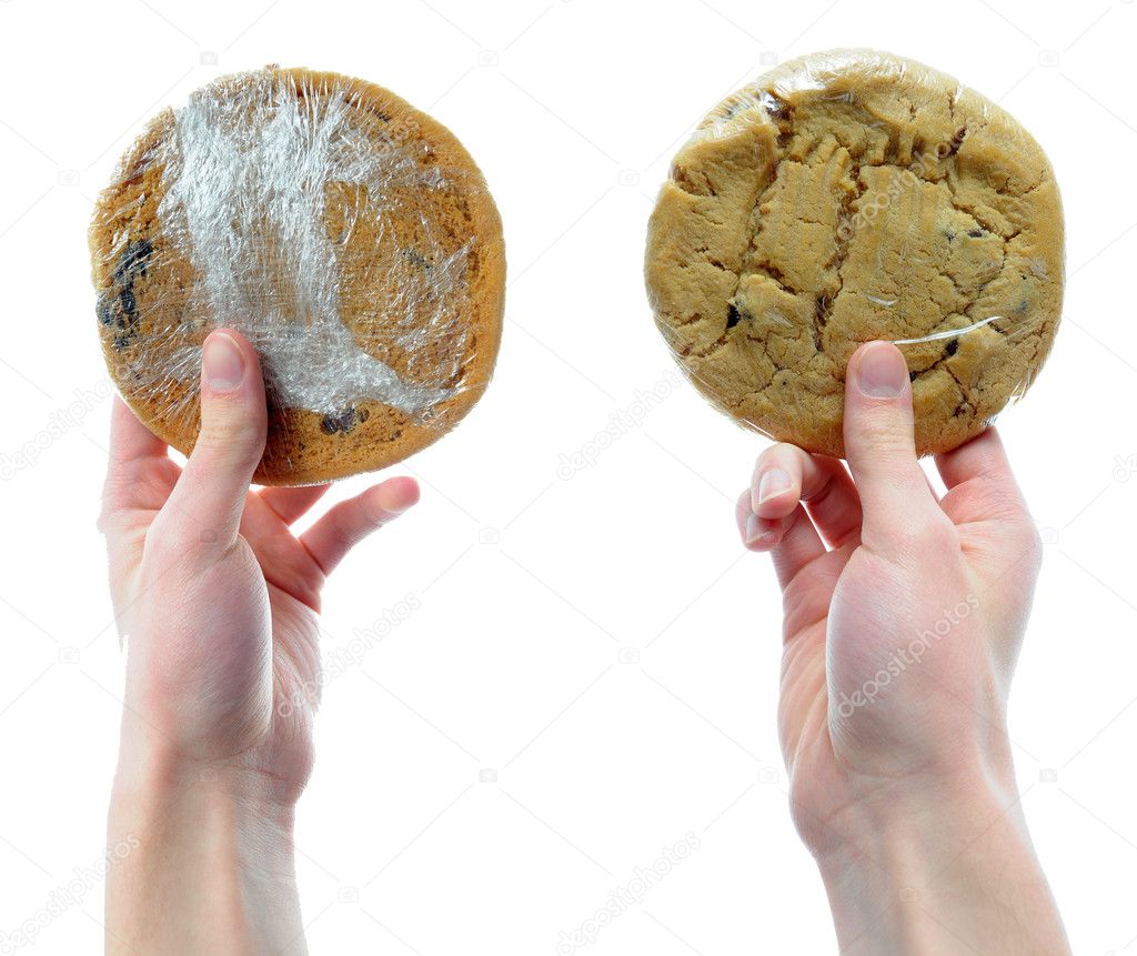 Two hands holding two cookies that are packaged n shrink plastic wrap isolated on a white background