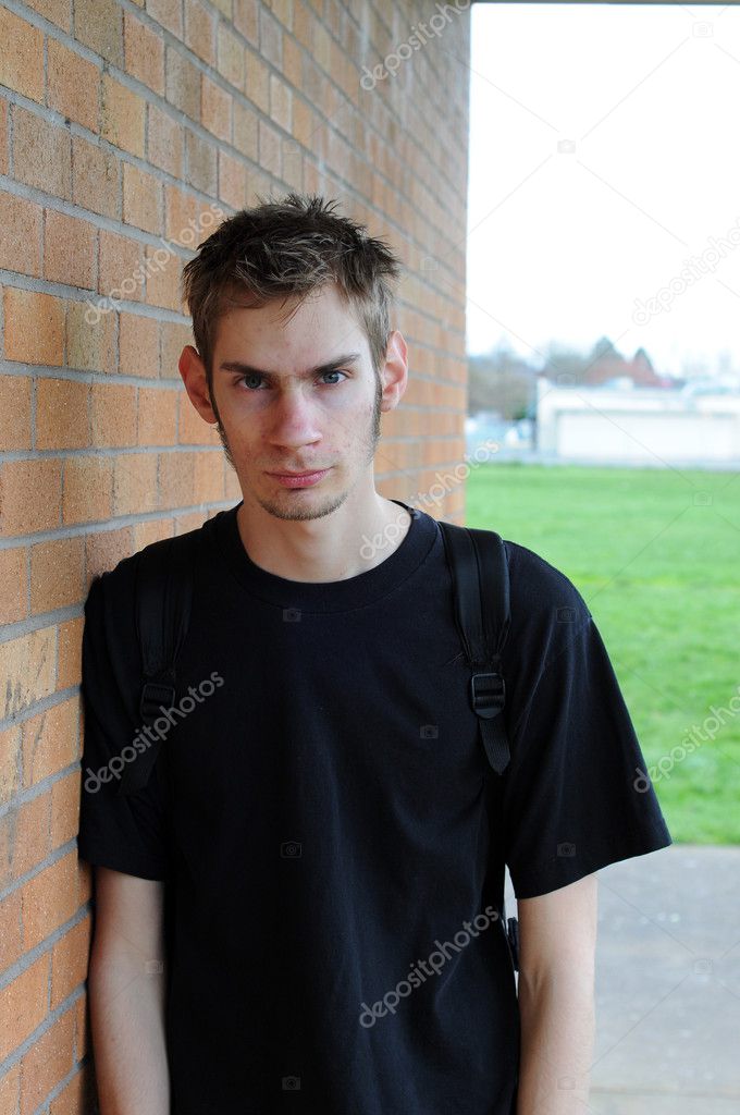 A healthy tall white male Caucasian student stands in front of a brick wall with his backpack on