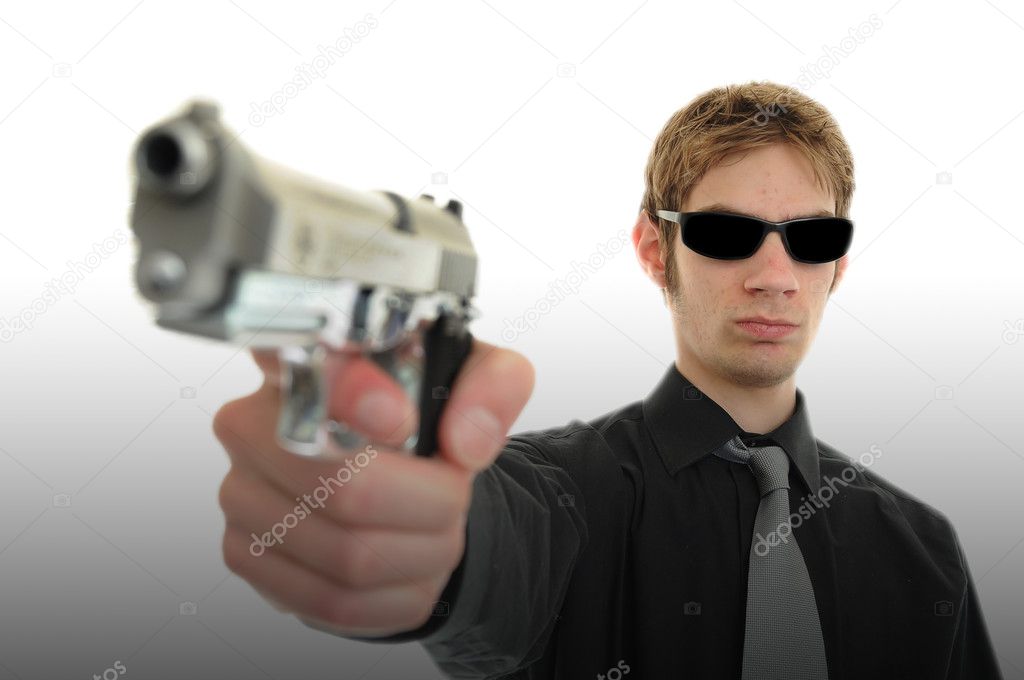 Young man holding up a gun with the focus on his face. He is wearing sunglasses and is isolated on white background cutout