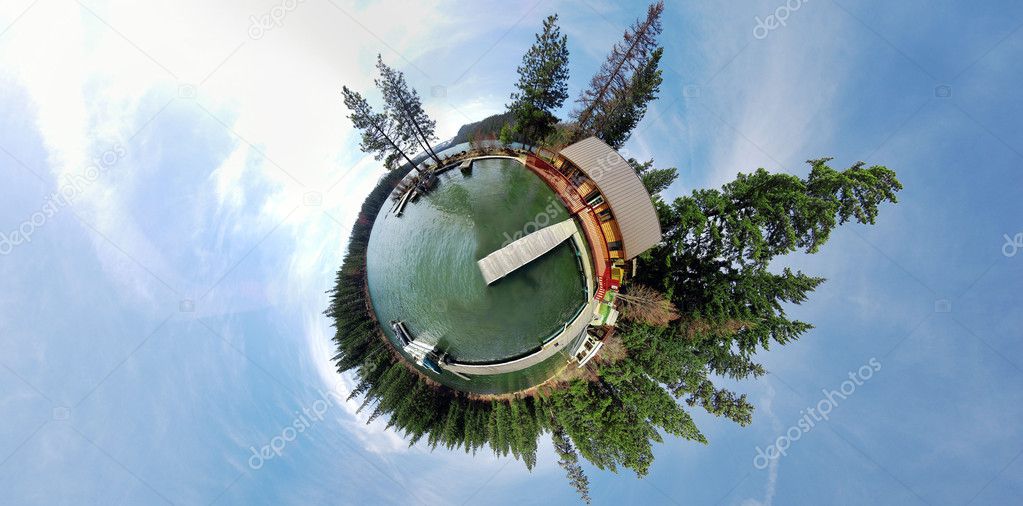 A 360x180 panoramic image projected to be in stereographic form. This is a pond with a dock, with trees and blue sky.