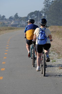 Two Bicyclists riding on a narrow road.