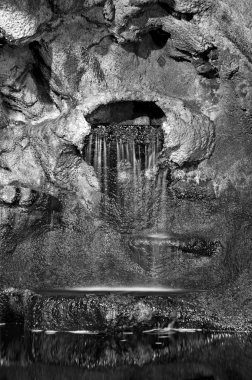 A waterfall spilling water onto a pond inside of a cave. clipart