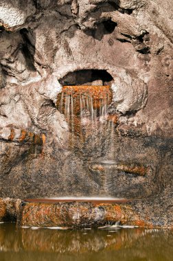 A waterfall spilling water onto a pond inside of a cave. clipart