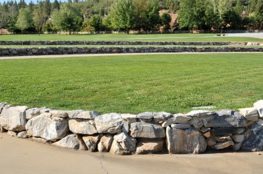 A modern amphitheater with grass and a rock wall during the day. clipart