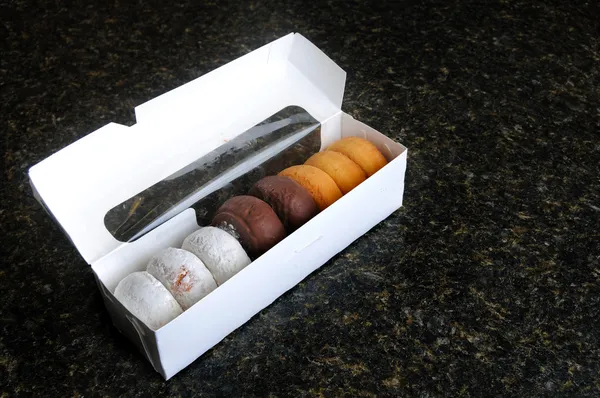 stock image An assortment of various donuts in a white box on a countertop.