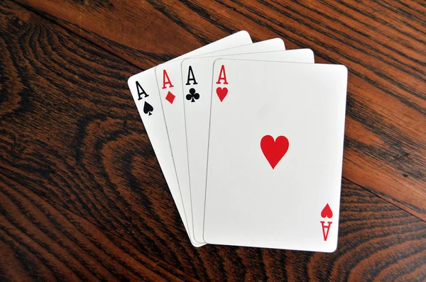 stock image A group of four playing card aces on a stained oak wooden table.