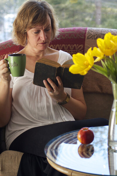 Mum takes some time out to read on a couch while sipping coffee