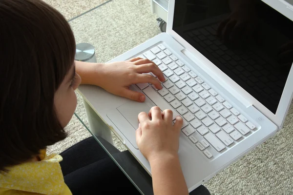 Little girl typing on a white laptop.