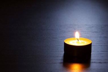 Single candle on a dark wooden table in back lit. Close up shot with selective focus.