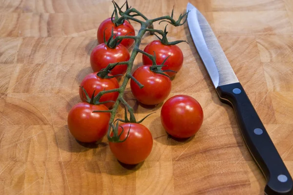 Stock image Ripe tomatoes on the vine resting on a wooden chopping board