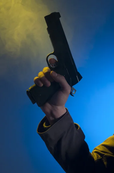 拿着枪 在蓝色背景 黄色光和黑烟的工作室拍摄的私家侦探 — 图库照片