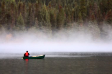 Man in canoe near morning mist on lake clipart