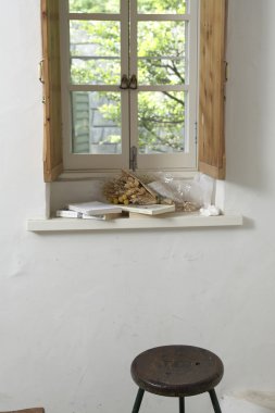 Books and dried flowers on window sill, wooden stool below clipart