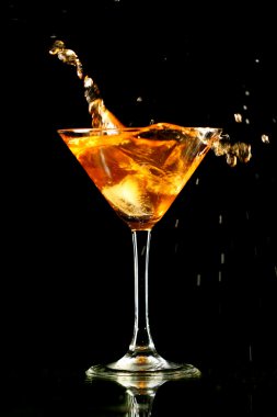 Alcohol splash in martini glass on black background clipart