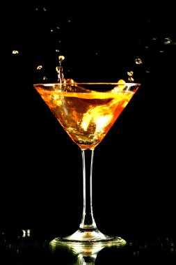 Alcohol splash in martini glass on black background clipart