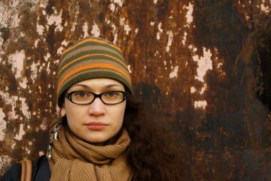 Beautiful young adult woman in a cap and glasses against a grungy rusty wall clipart