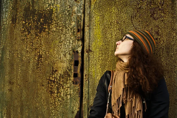 Beautiful young adult woman in a cap and glasses against a grungy rusty w — Stock Photo, Image