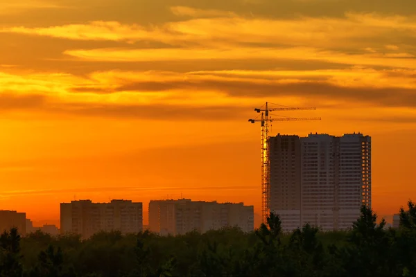 stock image Construction of a building, cranes and other machinery as silhouettes against a background of red sunset sky