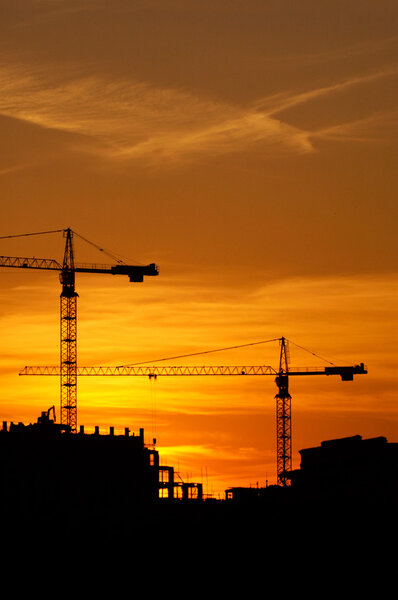Construction of a building, cranes and other machinery as silhouettes against a background of red sunset sky