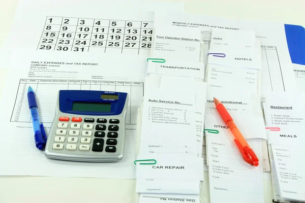 Picture of all expense report forms, daily and monthly, electronic calculator, pens and bills used to finalize financially the month - getting ready to fill dow