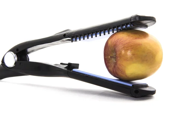 Jaws of a flat curling iron biting an apple — Stock Photo, Image