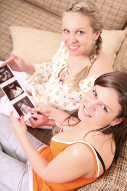 Happy pregnant woman and her freind is holding a sonogram of an unborn child clipart