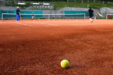 Kids are playing Tennis. A lonely Ball is lying in front of them. clipart