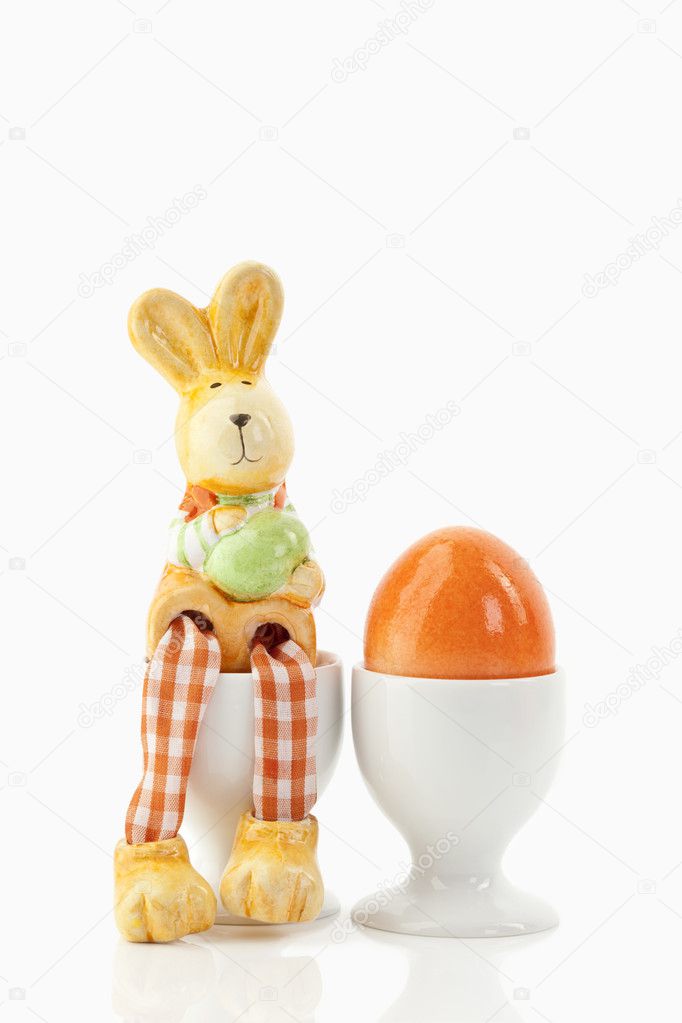 A easter bunny is sitting next to a colored egg in a cup
