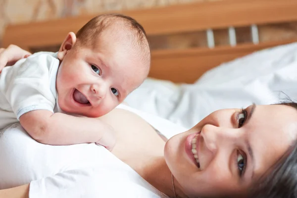 Ein lächelndes kleines Kind, das auf der Brust der Mutter liegt — Stockfoto