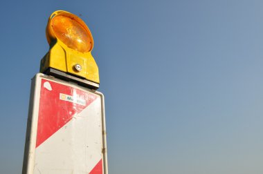Red and white striped road construction site marker against blue sky with yellow lamp clipart
