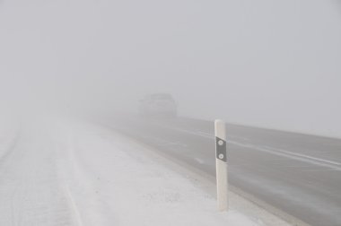 Auto im nebel auf einer Landstraße bei Winterwetter mit Schnee