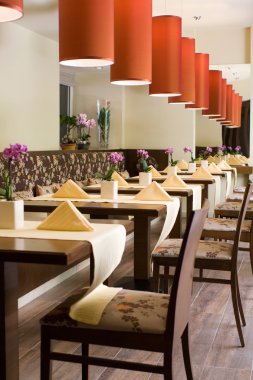 Interior of modern restaurant with the covered tables, wooden furniture, red lamps and flowers clipart