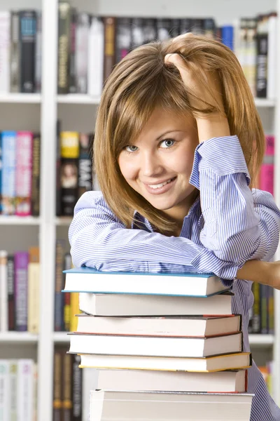 Giovane donna sorridente seduta con i libri in biblioteca — Foto Stock