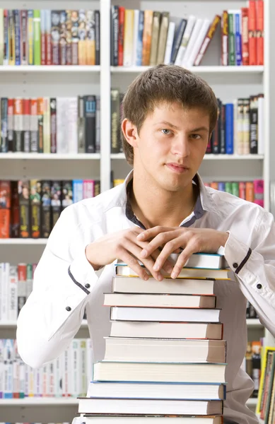Mladý muž sedí s knihami v knihovně — Stock fotografie