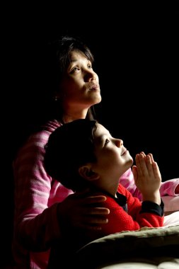 A woman says prayers with her son at bedtime. clipart