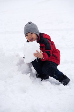 A little boy pretends like he is going to eat a big chunk of snow. clipart