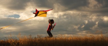 A panorama of a girl happily flying her kite. clipart