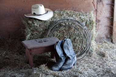 Some boots, a hat, a rope, and a bale of hay. clipart