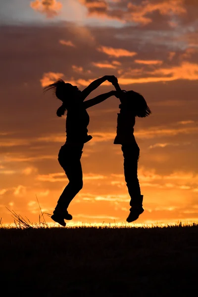 Mother and daughter leap at sunset. — Stock Photo, Image