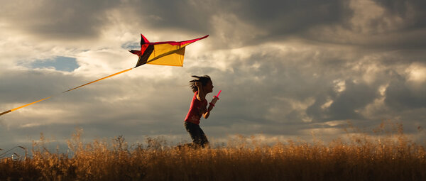 A panorama of a girl happily flying her kite.